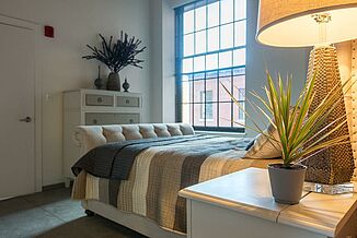 A bedroom in the Cable Mills residential complex. The room features natural light through the large, historic window.