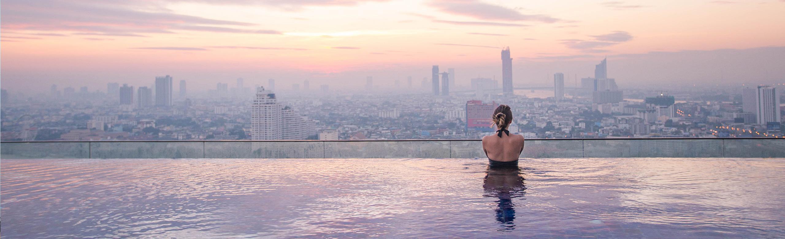 A woman stands in an infinity pool and looks at the city skyline.